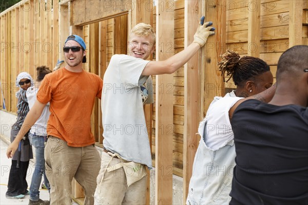 Smiling volunteers holding framed wall at construction site