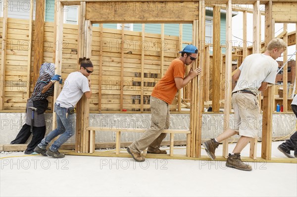 Volunteers pushing framed wall at construction site