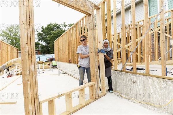 Smiling volunteers holding framed wall at construction site