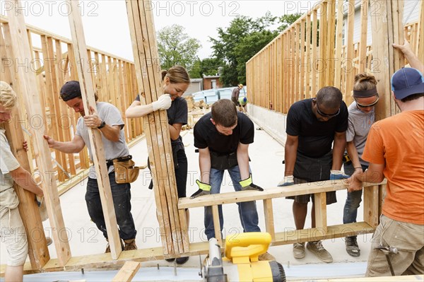 Volunteers lifting framed wall at construction site