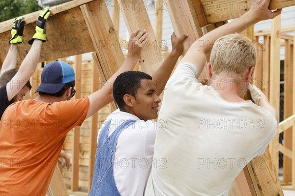 Volunteers lifting framed wall at construction site