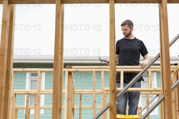 Caucasian man on ladder using hammer at construction site