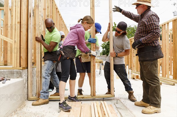 Volunteers lifting framed wall at construction site