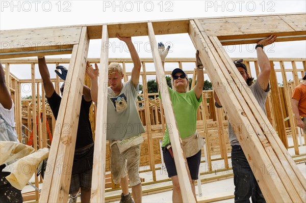 Volunteers lifting framed wall at construction site