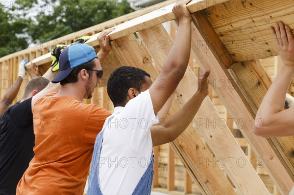 Volunteers lifting framed wall at construction site