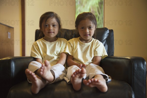 Mixed race twins with Down syndrome sitting in armchair