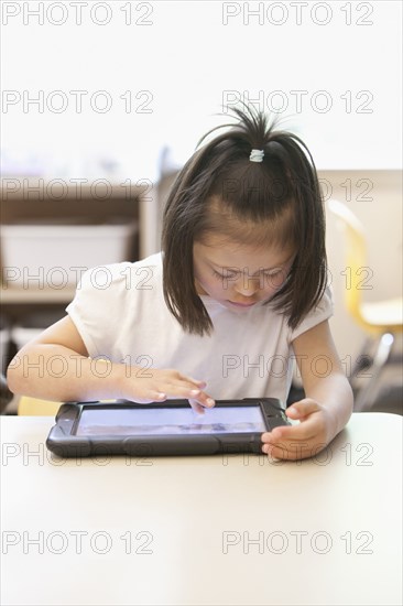 Mixed race Down syndrome student using tablet computer in classroom