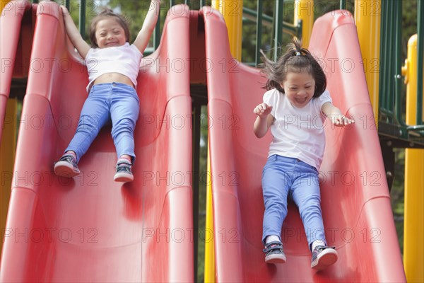 Mixed race Down syndrome girls playing on slides