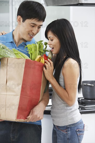 Asian couple looking in grocery bag in kitchen