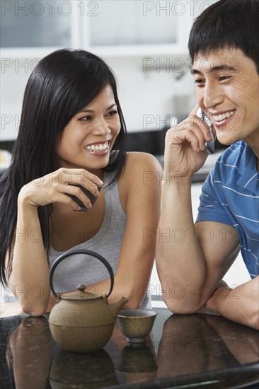 Asian couple having tea and using cell phone