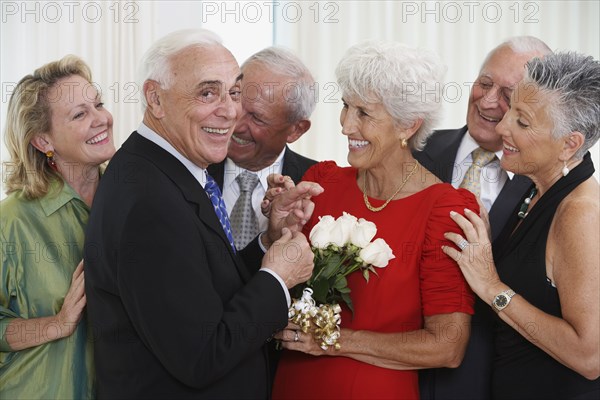 Senior man giving wife bouquet of flowers while friends watch