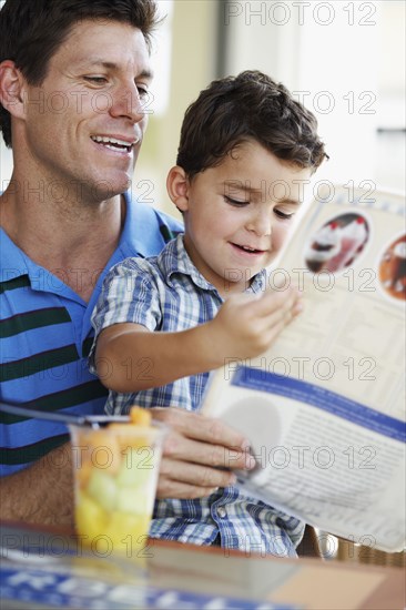 Hispanic father and son reading menu at restaurant