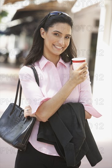 Hispanic businesswoman holding take out coffee