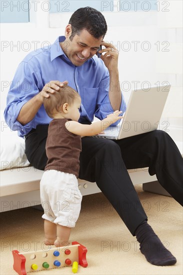 Hispanic father watching daughter and using laptop