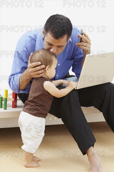 Hispanic father kissing daughter and using laptop