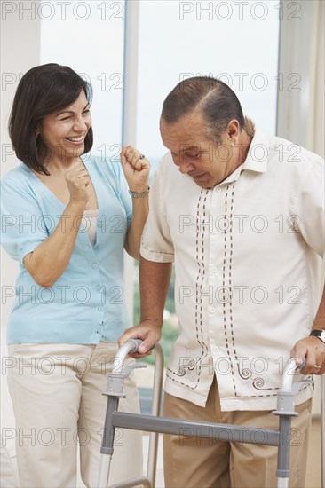 Hispanic woman watching husband use walker