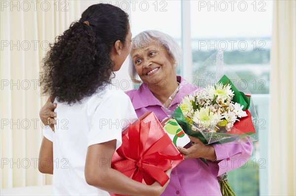 African American nurse giving senior woman flowers and gift
