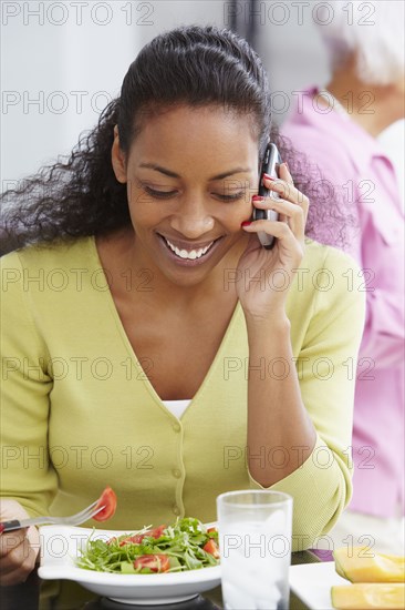 African American woman eating salad and talking on cell phone