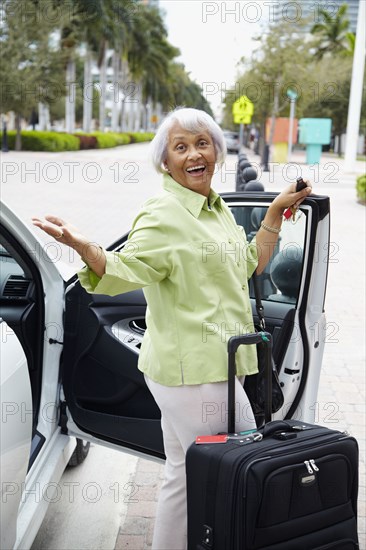 Senior African American woman standing with car and luggage