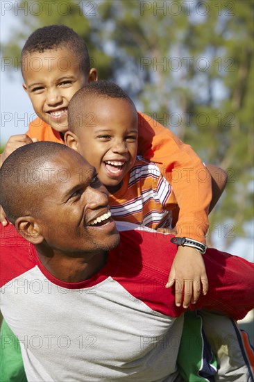 African American father giving sons piggy back ride