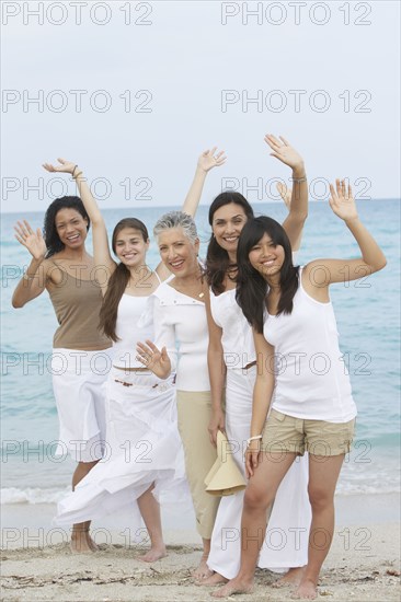 Diverse women standing on beach together waving