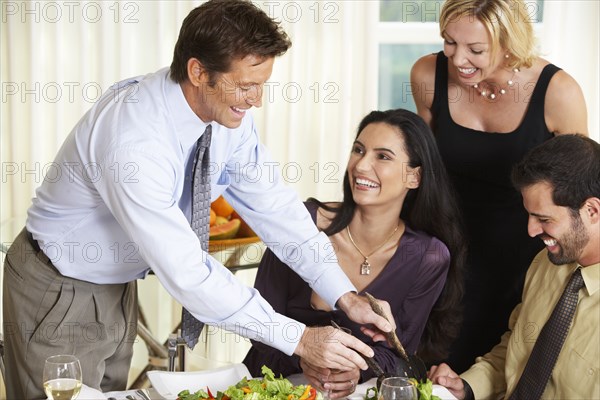 Man serving friends salad at dinner party