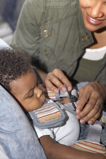 African American mother buckling baby into car seat