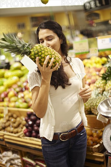 Hispanic woman smelling pineapple in grocery store