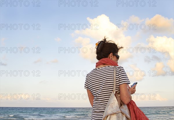 Caucasian woman holding cell phone on beach