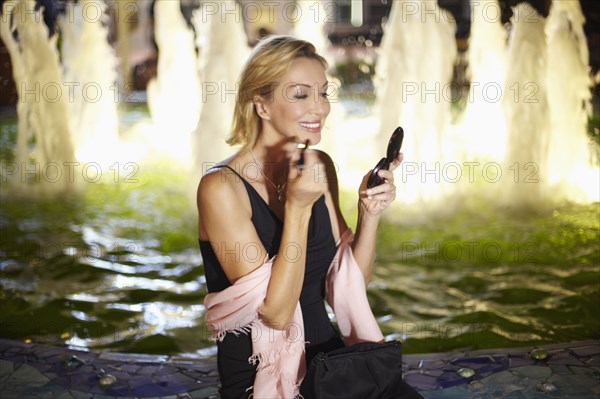 Caucasian woman putting on make up near fountain