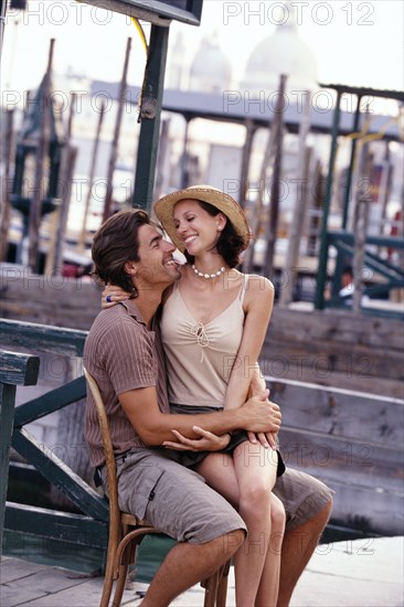 Caucasian couple sharing chair on city street