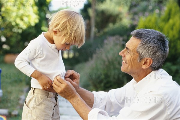 Caucasian father buttoning son's shirt outdoors