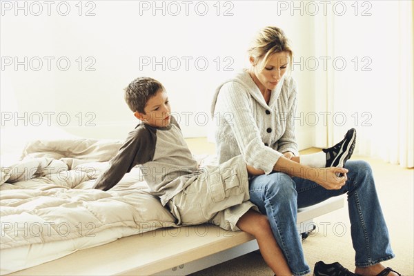 Mother putting son's shoes on on bed