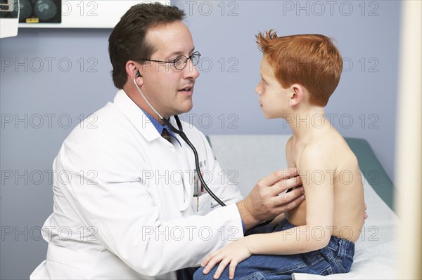 Doctor listening to boy's heartbeat in office