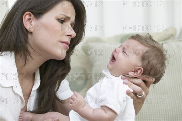 Mother comforting crying baby on sofa