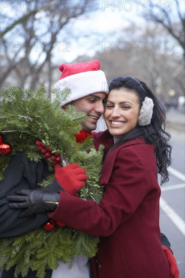 Couple carrying Christmas wreath on city street