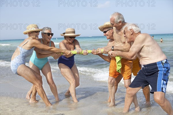 Senior friends playing tug-of-war on beach