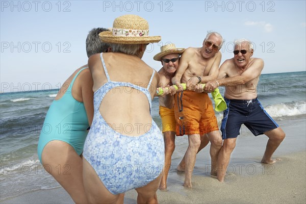 Senior friends playing tug-of-war on beach