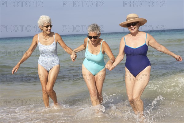 Senior women walking in waves on beach