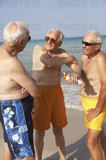 Senior men applying sunscreen on beach