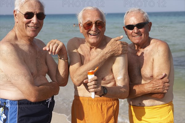 Senior men applying sunscreen on beach