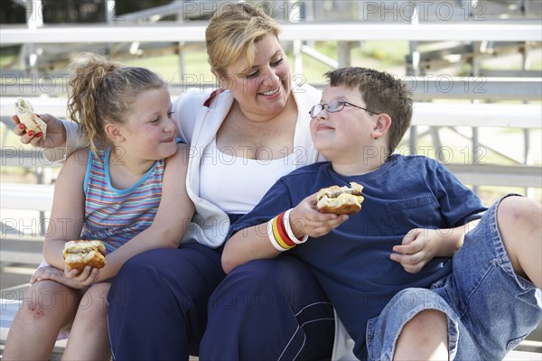 Mother and children eating sandwiches on bleachers