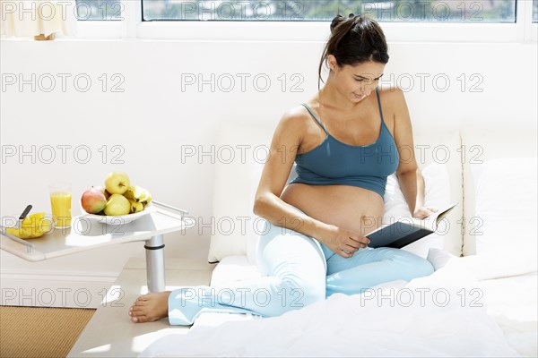 Pregnant Hispanic woman reading in bed