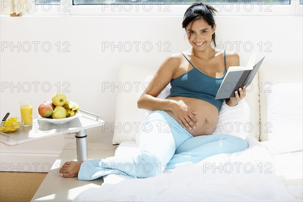 Pregnant Hispanic woman reading in bed