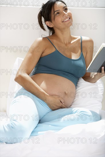 Pregnant Hispanic woman reading in bed