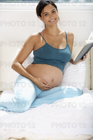 Pregnant Hispanic woman reading in bed