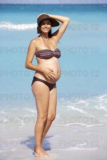 Pregnant Hispanic woman standing on beach