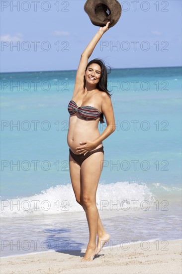 Pregnant Hispanic woman cheering on beach