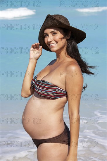 Pregnant Hispanic woman smiling on beach