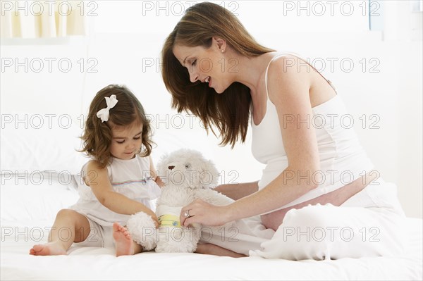 Caucasian mother and daughter playing with teddy bear
